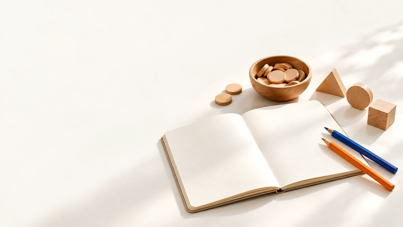 A blank notebook, pencils, wooden counters and geometric shapes for math practice